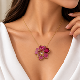 Pink Pavé Flower Pendant Necklace Gold Fuchsia Pear Crystal - pendant macro flat lay on cream satin: large five-petal botanical flower pendant showing full hot pink pavé crystal petal surface with warm gold borders, raised gold stamen centre with square white crystal in crown prong setting, large pear deep fuchsia-ruby crystal solitaire in pavé pink halo setting on upper right petal