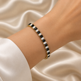 Black and White Baguette Tennis Bracelet Gold Alternating Crystal - vertical macro flat lay on cream satin: close view of full bracelet length standing vertically showing strict alternating jet black and clear white baguette crystal zirconia stones in individual warm 18K gold four-prong claw settings, uninterrupted black-white alternating sequence