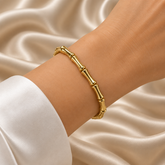 Gold Bamboo Bangle Bracelet Mirror Polish Sculptural - hero flat lay on cream satin: full bangle in circular form showing complete bamboo motif with smooth mirror-polish warm 18K gold tube sections and double-ring node joints alternating around full circumference, warm gold reflective surface on cream satin background
