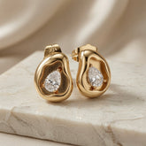 Molten Pear Crystal Stud Earrings - pair angled view showing pear crystal in sand-textured gold crater on marble