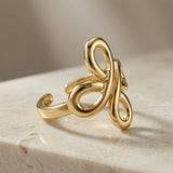 Infinity Bloom Gold Ring - angled three-quarter view on travertine showing full sculptural form and mirror polish