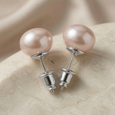 Perle Blush Pearl Stud Earrings Silver - pair on travertine showing blush pearl and silver cup setting and screw-back detail