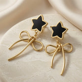 Étoile Noir Bow Drop Earrings - pair on marble disc showing black enamel star studs and sculptural gold wire bow drops