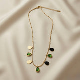Pluie Verte Charm Necklace Black & Emerald - flat lay on ivory silk showing black enamel and emerald crystal teardrop charm colourway