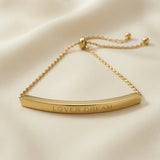Lover Dream Curved Bar Bolo Bracelet - macro flat lay on ivory silk showing LOVER DREAM capital letter engraving in full detail on mirror-polished curved gold bar