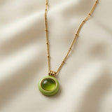 Pistache Cabochon Pendant Necklace - close-up on ivory silk showing pistachio enamel circular pendant and domed olive cabochon crystal