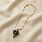 Coeur Noir Pendant Necklace - flat lay on ivory silk showing glossy black enamel 3D puffy heart with gold drip fang tips on flat snake chain
