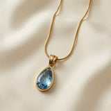Larme Crystal Pear Pendant Necklace Aquamarine - close-up on ivory silk showing double-ridged gold bail, continuous bezel and aquamarine crystal facets
