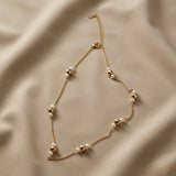 Perle Dorée Station Necklace - full flat lay on taupe silk showing alternating faceted gold disco beads and freshwater pearls on cable chain