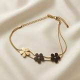 Trois Fleurs Double Snake Chain Bracelet Gold & Noir colourway - flat lay on ivory silk showing one gold daisy and two matte black daisy flowers with crystal centres on double gold snake chain