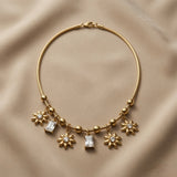Soleil Baguette Fringe Charm Set necklace - flat lay on taupe silk showing round snake chain with alternating gold ball and rope barrel stations, three sculptural eight-petal gold sunflower charms with crystal centres alternating with two baguette crystal zirconia drops in four-prong gold mounts, lobster clasp