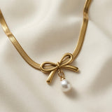 Trois Noeuds Pearl Herringbone Necklace - close-up on ivory silk showing single gold bow with freshwater pearl drop on wide flat herringbone chain