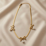 Trois Noeuds Pearl Herringbone Necklace - full flat lay on ivory silk showing complete herringbone chain, lobster clasp, curb extender and three bow pearl drop composition
