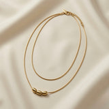 Trio Ovale Double Layer Snake Chain Necklace - flat lay on ivory silk showing both snake chains from single lobster clasp, curb extender and three gold oval barrels