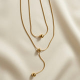 Sphère Lariat Double Layer Snake Chain Necklace - close-up flat lay on ivory silk showing sliding sphere mechanism, station sphere and lariat drop with terminating gold ball