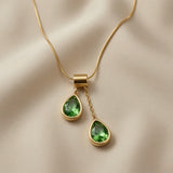 Duo Larme Émeraude Asymmetric Pendant Necklace - close-up on ivory silk showing rectangular bail, upper pear crystal on jump ring and lower pear crystal on cable chain drop with emerald green facets