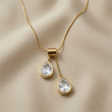 Duo Larme Crystal Asymmetric Pendant Necklace - close-up on champagne silk showing rectangular gold bail, upper white crystal pear on jump ring and lower pear on cable chain drop