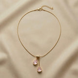 Duo Larme Rose Asymmetric Pendant Necklace - full flat lay on champagne silk showing complete snake chain with lobster clasp extender, rectangular gold bail and two asymmetric blush rose pear crystal pendants
