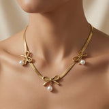 Trois Noeuds Pearl Herringbone Necklace - worn on mannequin collarbone showing three gold bows and three pearl drops fanning across chest on wide flat herringbone chain