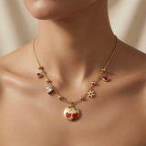 Cerise Charm Station Necklace - worn on mannequin collarbone showing cherry medallion at chest centre, four satellite charms fanning across collarbone on gold ball station snake chain