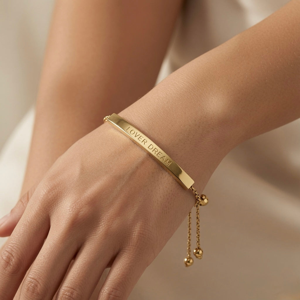 Lover Dream Curved Bar Bolo Bracelet - worn on model wrist showing curved gold bar lying flat against inner wrist with LOVER DREAM inscription reading against warm skin, bolo slider and gold ball tails at back of wrist