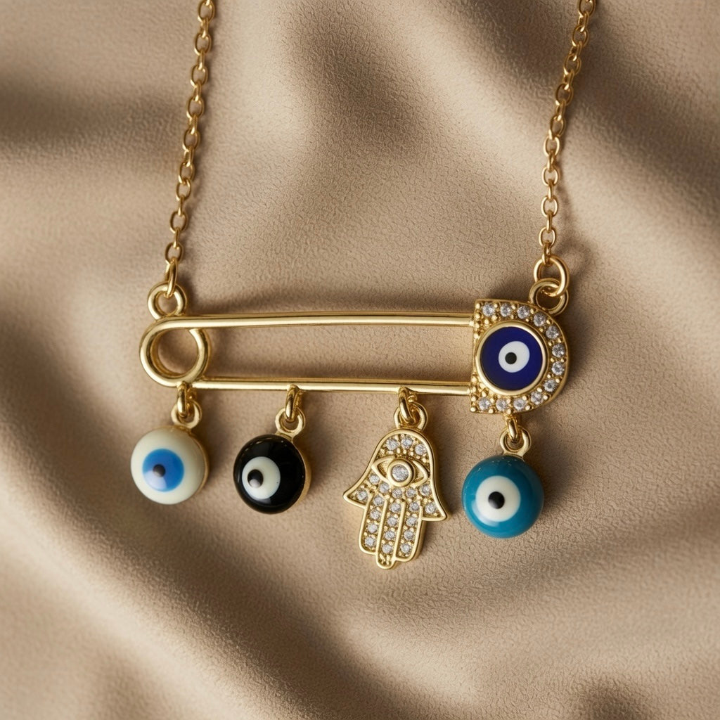 Nazar Pin Charm Necklace - macro close-up on taupe silk showing large gold safety pin with navy blue evil eye disc in pavé crystal zirconia halo at clasp end, white enamel evil eye bead, black enamel evil eye bead, pavé crystal Hamsa hand with evil eye at palm and turquoise enamel evil eye bead sliding on pin bar