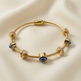 Nazar Cable Wire Evil Eye Station Bangle - close-up flat lay on ivory silk showing twisted gold cable wire bangle detail with deep blue evil eye disc stations showing navy blue iris, white ring and black pupil in gold barrel bezels, crystal pavé rondelle stations with brilliant-cut crystal zirconia and gold disc collars, gold barrel magnetic clasp