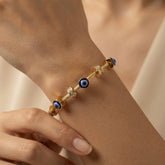 Nazar Cable Wire Evil Eye Station Bangle - worn on model wrist showing three deep blue evil eye disc stations watching outward from front, left and right of wrist simultaneously, alternating with three crystal pavé rondelle stations on twisted gold cable wire bangle against warm skin