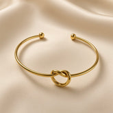 Nœud d’Amour Love Knot Ball-End Cuff Bangle - three-quarter view on ivory silk showing love knot detail at base of smooth round-wire gold open cuff bangle with two polished gold ball finials at open ends, warm 18K gold mirror-polish surface
