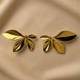 Feuilles d’Or Multi-Leaf Cluster Stud Earrings - pair front flat lay on champagne silk showing both five-leaf cluster stud earrings in warm 18K gold: one large dominant leaf extending horizontally outer, one medium leaf upward outer, one small pointed leaf top centre, two narrow leaves fanning downward, all radiating from single central point with deep shadow recesses between leaves