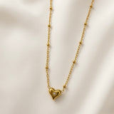Étoile du Cœur Puffy Heart Satellite Chain Necklace - close-up flat lay on ivory silk showing three-dimensional puffy heart pendant in warm 18K gold with single round brilliant crystal zirconia in eight-point star sunburst bezel setting at centre of heart face, fine satellite chain with smooth gold ball stations visible on both sides