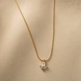 Tulipe Blanche Crystal Bud Pendant Necklace - three-quarter view on warm beige background showing complete white tulip pendant on twisted cable chain: pear-cut diamond-clear white crystal bud above two white marquise crystal leaves on fine gold stem, pure white crystal brilliance of both bud and leaves clearly visible against warm gold chain and stem