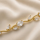 Diamant Vigne Wave Link Crystal Bracelet - macro close-up on champagne silk showing three links in detail: large oval brilliant-cut white crystal zirconia in four-prong ball-tip gold setting at centre showing diamond-like white brilliance and facet detail, paired marquise navette white crystal zirconia in two-prong point-tip settings on sinuous S-curve gold wave links, warm gold ball-tip prong detail clearly visible