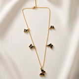 Papillon Noir Black Enamel Butterfly Charm Necklace - full length flat lay on ivory silk showing complete necklace laid out: fine gold oval-link cable chain with five graduated black enamel butterfly charms at asymmetric intervals showing size graduation from small upper butterflies to large central drop, lobster clasp at top, deep black enamel fill with warm gold border on each butterfly charm clearly visible