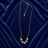 Lumière Cinq Cushion Crystal Convertible Snake Chain Necklace - full flat lay on deep navy velvet in station mode showing complete necklace: flat-link gold snake chain with five cushion-cut diamond-clear crystal zirconia in smooth gold bezels arcing across front, gold bar-and-ball toggle at left, lobster clasp and branded extender chain tag at top right