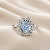 Sky Blue Crystal Snowflake Halo Ring - face-on on ivory satin showing complete ring: round pale sky blue crystal zirconia centre stone in multi-prong setting surrounded by dramatic double starburst halo of round brilliant white crystal zirconia stones and polished silver ball details radiating in snowflake pattern, plain polished round-wire silver band