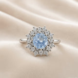 Sky Blue Crystal Snowflake Halo Ring - face-on on ivory satin showing complete ring: round pale sky blue crystal zirconia centre stone in multi-prong setting surrounded by dramatic double starburst halo of round brilliant white crystal zirconia stones and polished silver ball details radiating in snowflake pattern, plain polished round-wire silver band