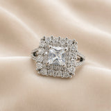 Princess Cut Double Halo Split Shank Adjustable Ring - face-on on ivory satin showing complete double halo composition: princess-cut diamond-clear white crystal zirconia centre in four-prong setting, inner halo of individually prong-set round brilliant white crystals in square arrangement, outer halo of larger round brilliant white crystals in outer square arrangement, split shank pavé band visible below