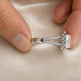 Princess Cut Double Halo Split Shank Adjustable Ring - held between fingers on ivory satin showing split shank band construction and elevated gallery: split shank double-rail pavé band clearly showing two parallel micro-pavé rails converging at base of head, elevated square gallery platform with baguette accent stones on sides of centre stone, princess cut centre stone at top