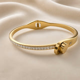 Side view of gold-tone bangle bracelet with clear crystal-style details and structured clasp
