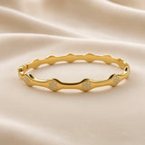 Gold-tone bangle bracelet showing its scalloped wave design and clear accent stones