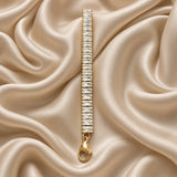 Baguette Crystal Tennis Bracelet Gold - diagonal flat lay on cream satin showing full baguette channel band detail: step-cut white crystal zirconia stones in continuous channel setting, lobster clasp with gold tag at bottom