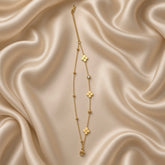 Gold Clover and Crystal Station Bracelet Satellite Chain - vertical flat lay on cream satin: fine gold cable chain with nine inline stations, three flat mirror-polish gold four-petal clover stations clustered at centre, two round white crystal zirconia bezel stations at outer positions, four small gold ball satellites flanking crystal bezels, lobster clasp at base with curb extender chain at top