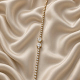 Double Pear Crystal Tennis Bracelet Gold Round Bezel - vertical flat lay on cream satin: full tennis chain of continuously bezel-set round brilliant white crystal zirconia stones in circular gold bezels, double pear crystal centre accent with two side-by-side pear cut white crystals in open claw settings at centre, pointed tips descending