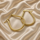 Gold Teardrop Hoop Earrings Tube Round Section Mirror Polish Latch Back Clasp - angled pair flat lay on cream satin: pair of teardrop hoops shown at angle with hoops overlapping, showing three-dimensional round tubular cross-section of hoop body, mirror-polish warm gold surface from multiple angles, latch-back clasp with straight post open at left earring, cream satin background