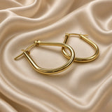 Gold Teardrop Hoop Earrings Tube Round Section Mirror Polish Latch Back Clasp - single earring hero detail on cream satin: single teardrop tube hoop earring showing complete elongated pear teardrop silhouette from rounded base through full tubular round-section hoop body to hinged latch-back clasp at top with barrel hinge detail and straight post visible, mirror-polish warm 18K gold surface catching light as rolling warm gold specular highlight across tube body, cream satin background