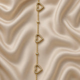 Gold Open Pavé Heart Charm Bracelet Bezel Crystal Station Chain - overhead flat lay on cream satin: full bracelet in circular form showing three open micro-pavé white crystal zirconia heart charms and two round bezel crystal stations on fine warm 18K gold cable chain, lobster clasp at top, cream satin background