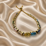 Gold Multi-Colour Emerald Cut Crystal Tennis Bracelet Bolo Adjustable Slider - on wrist lifestyle: bracelet worn on warm-toned wrist with white satin sleeve, continuous multi-colour emerald-cut crystal tennis line sitting flat across wrist showing yellow citrine, sapphire blue, peridot green, and rose pink cycling colour palette in warm gold box settings, bolo slider and gold ball tips at wrist side, white satin background