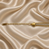 Gold Three Row Bracelet Crystal Tennis Centre Ball Bead Chain Lobster Clasp - on wrist lifestyle: bracelet worn on warm-toned wrist with white satin sleeve, wide three-row construction sitting across wrist showing smooth upper and lower warm gold ball bead rows flanking centre round brilliant white crystal tennis row, tapered shield end cap and extension chain at wrist side, white satin background