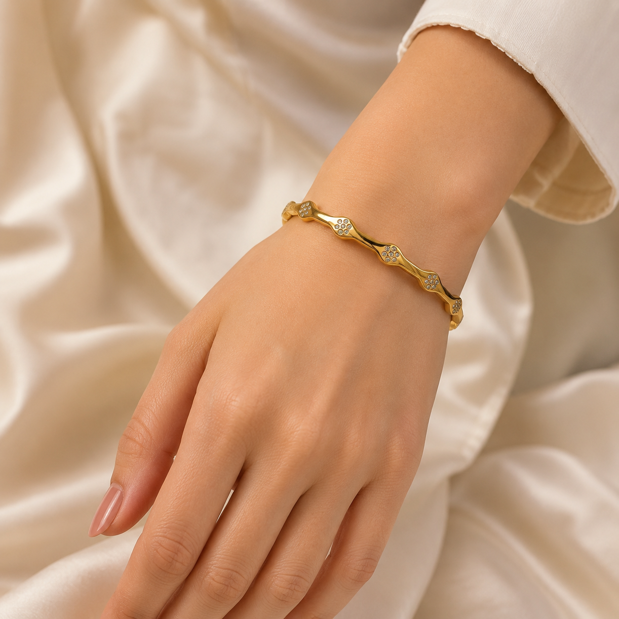 Gold-tone wave bangle bracelet with clear crystal-style accents on beige fabric